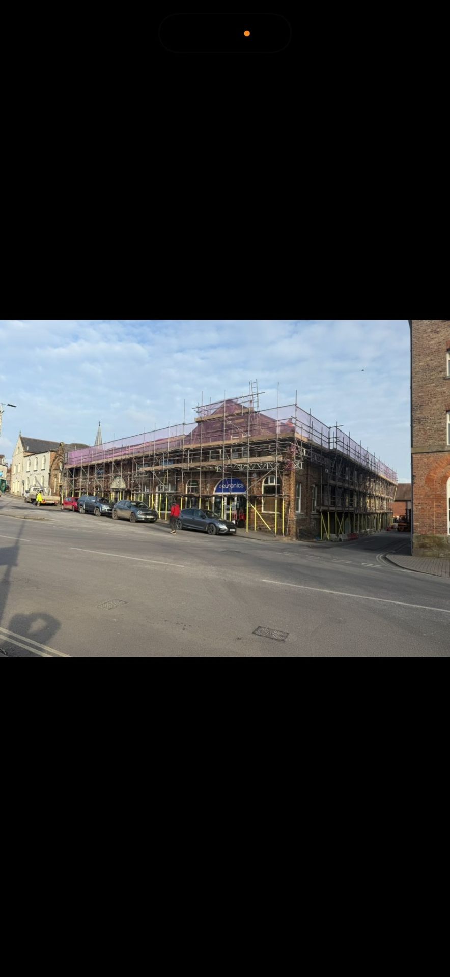 Commercial corner building in York with full perimeter scaffolding and pink safety sheeting at roof level