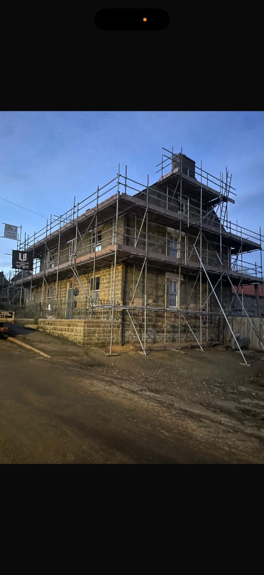 Yorkshire stone house at dusk with full perimeter scaffolding and LB Scaffolding Ltd banner
