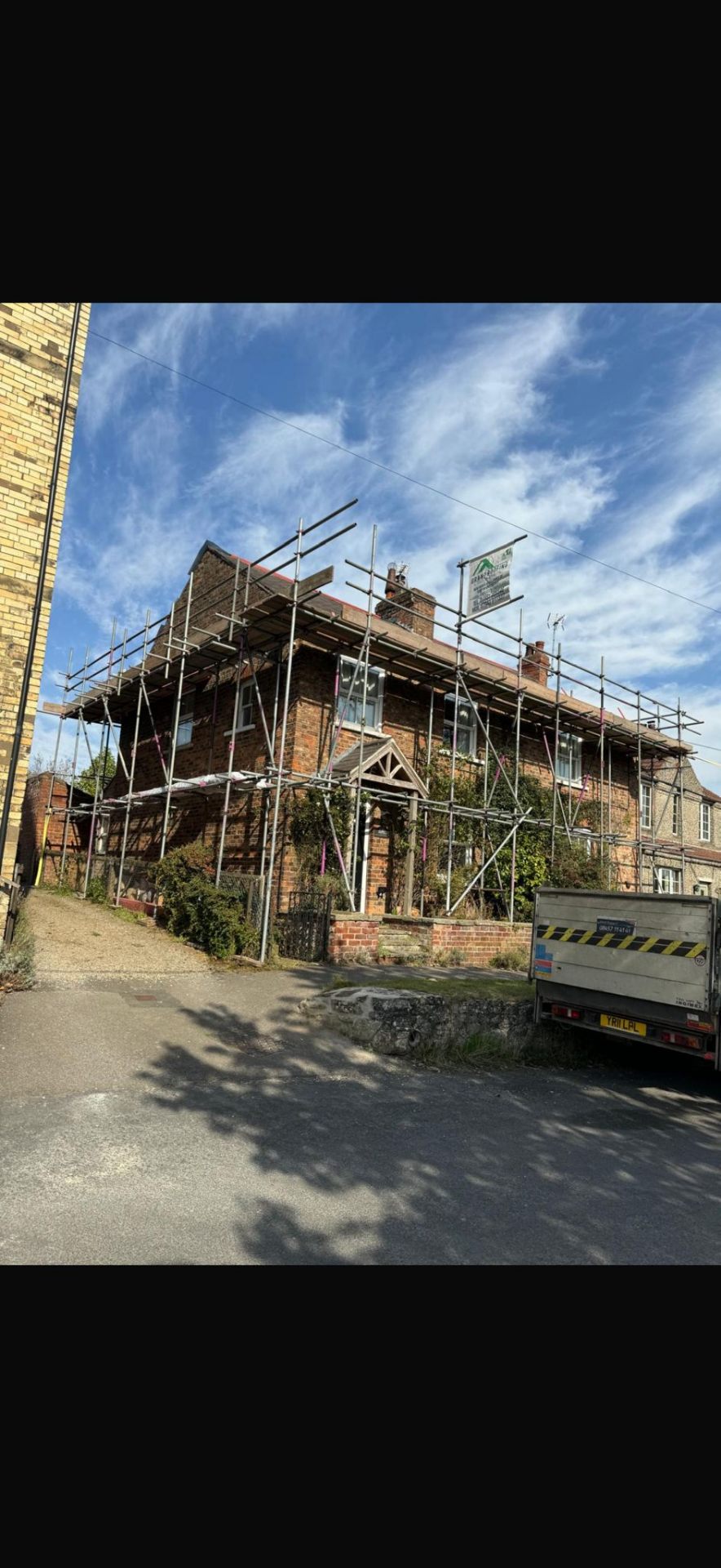 Red-brick semi-detached home with scaffolding around the gable and roof line