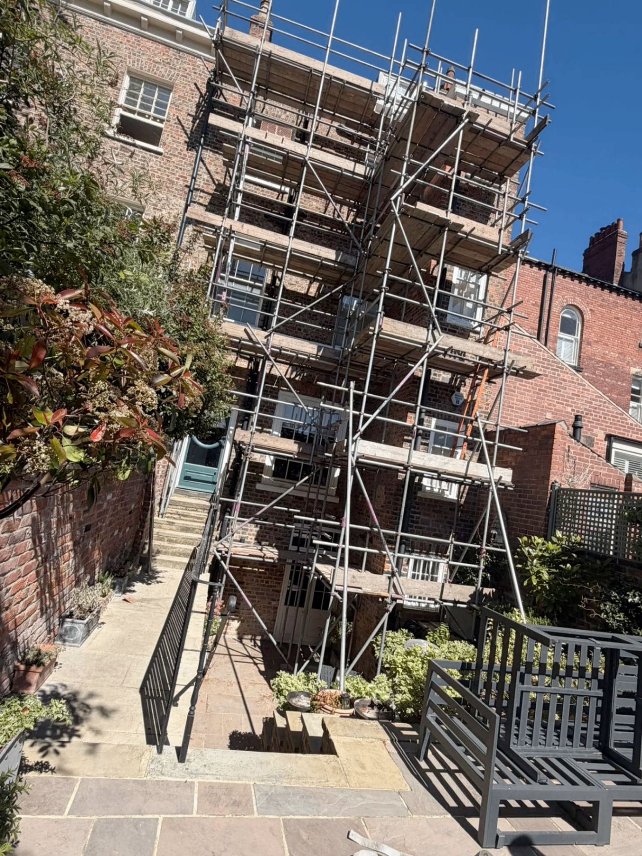 Rear elevation of a Georgian brick townhouse with multi-lift scaffolding rising above a garden patio