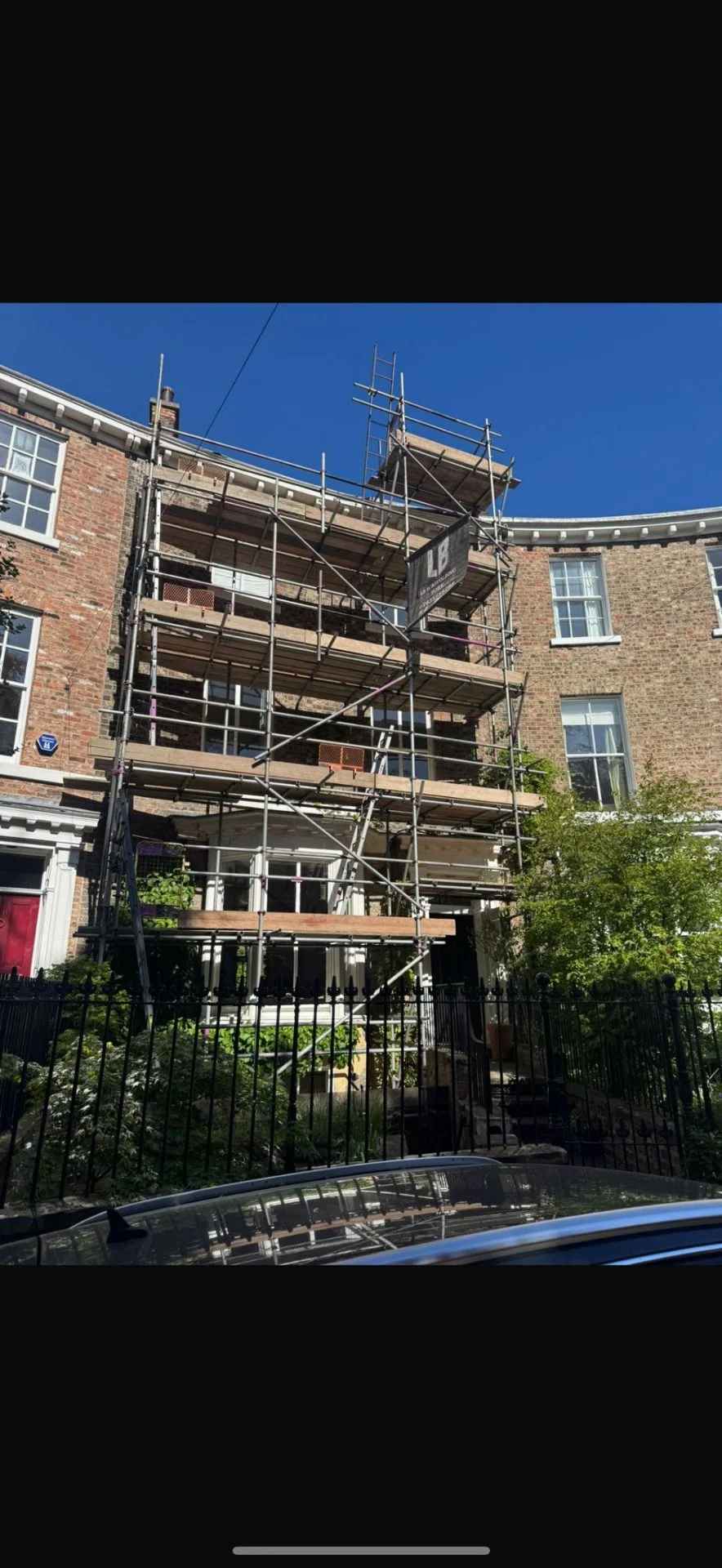 Curved brick terrace with multi-lift scaffolding and LB Scaffolding Ltd banner facing the street