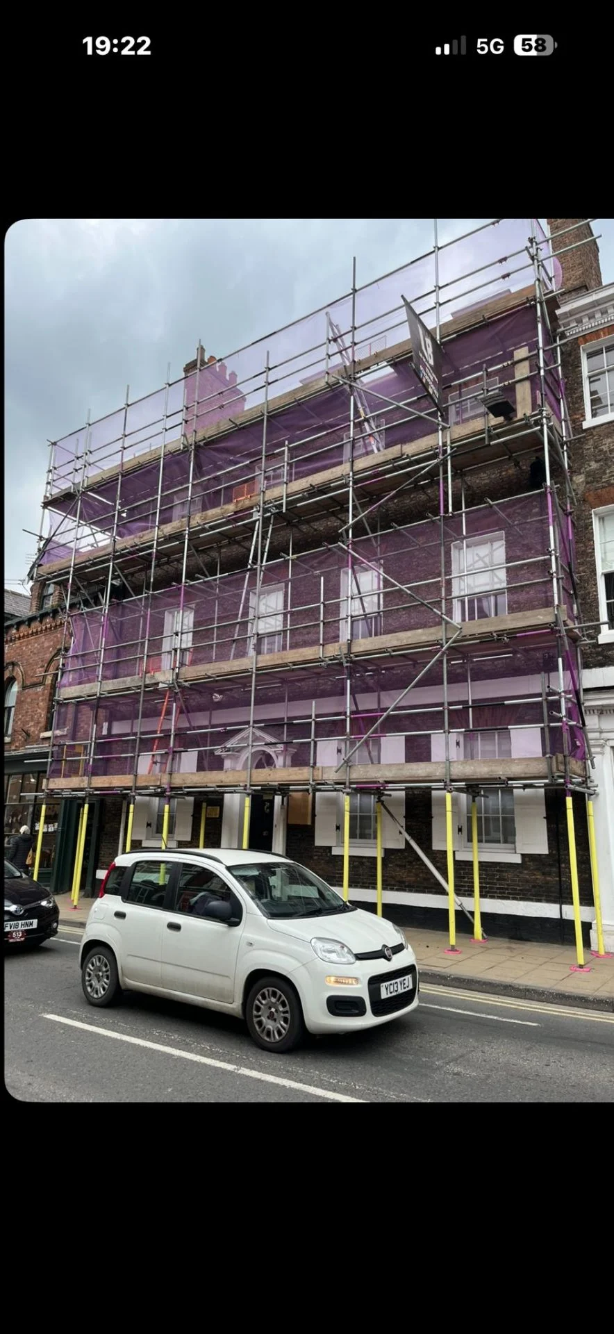 York high-street commercial building with three-lift scaffolding wrapped in pink safety sheeting
